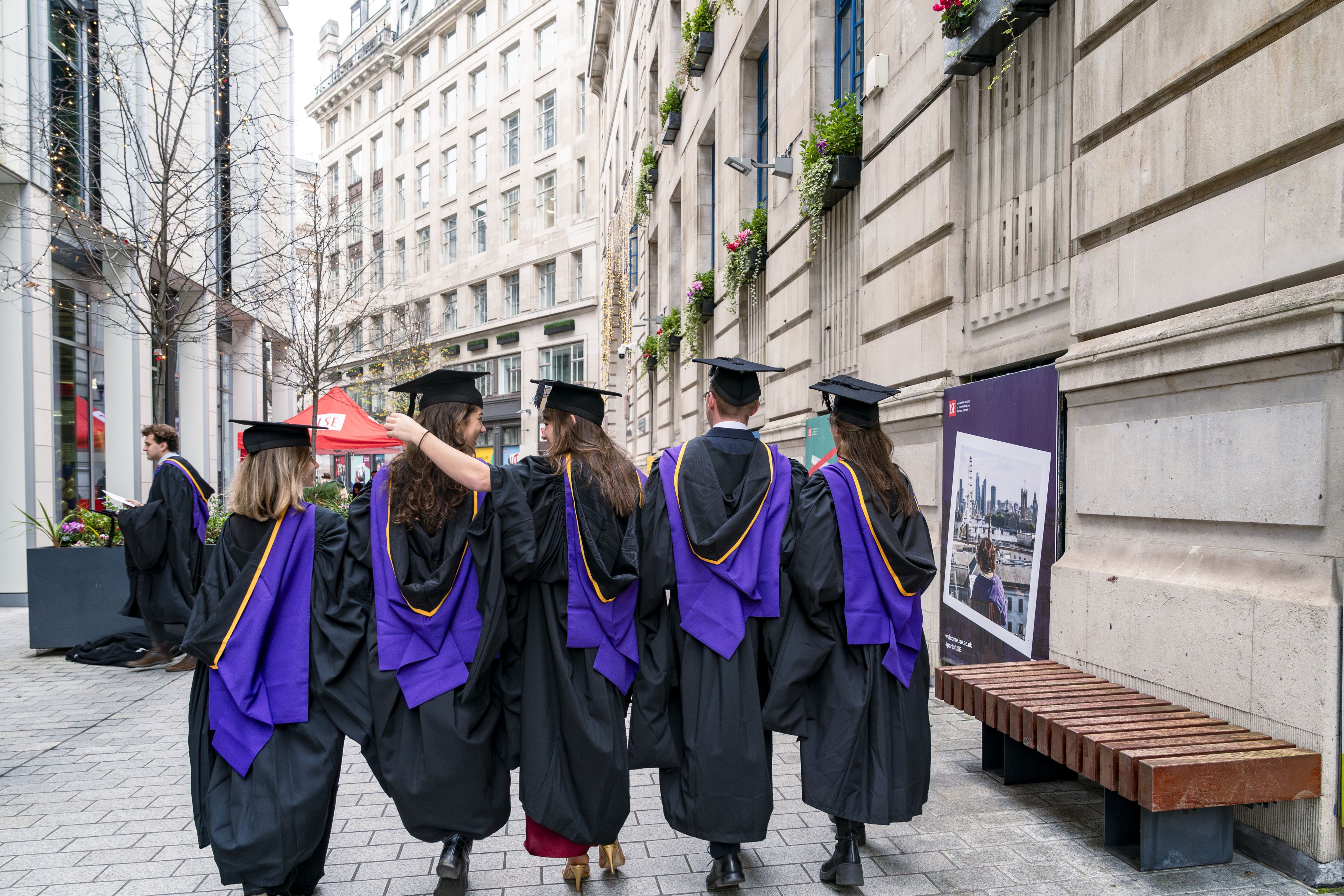 Group of five graduates on campus walking away from camera 