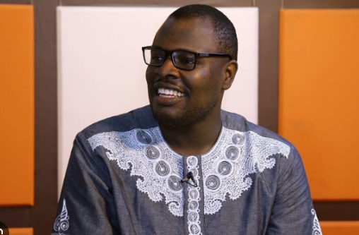 Chude Jideonwo sitting in front of an orange, black and white background