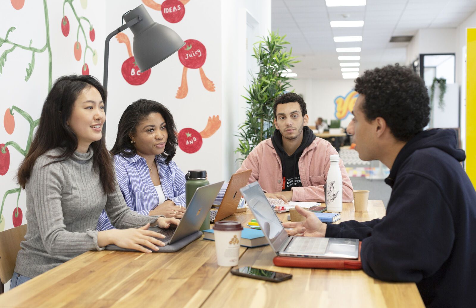 A group of four LSE students with laptops talking in an LSE Generate space