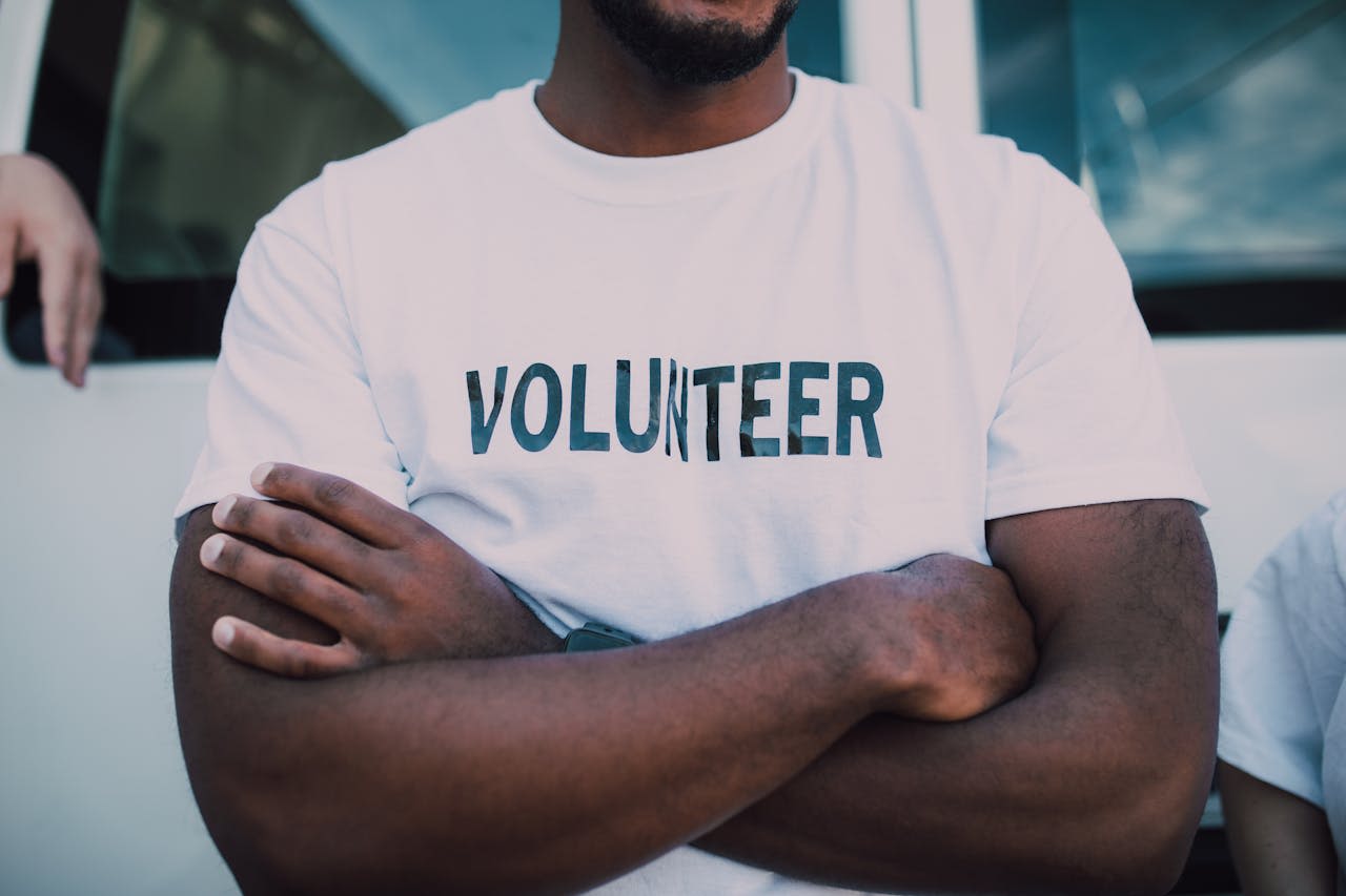 A person crossing their arms, wearing a t-shirt that says 'volunteer'