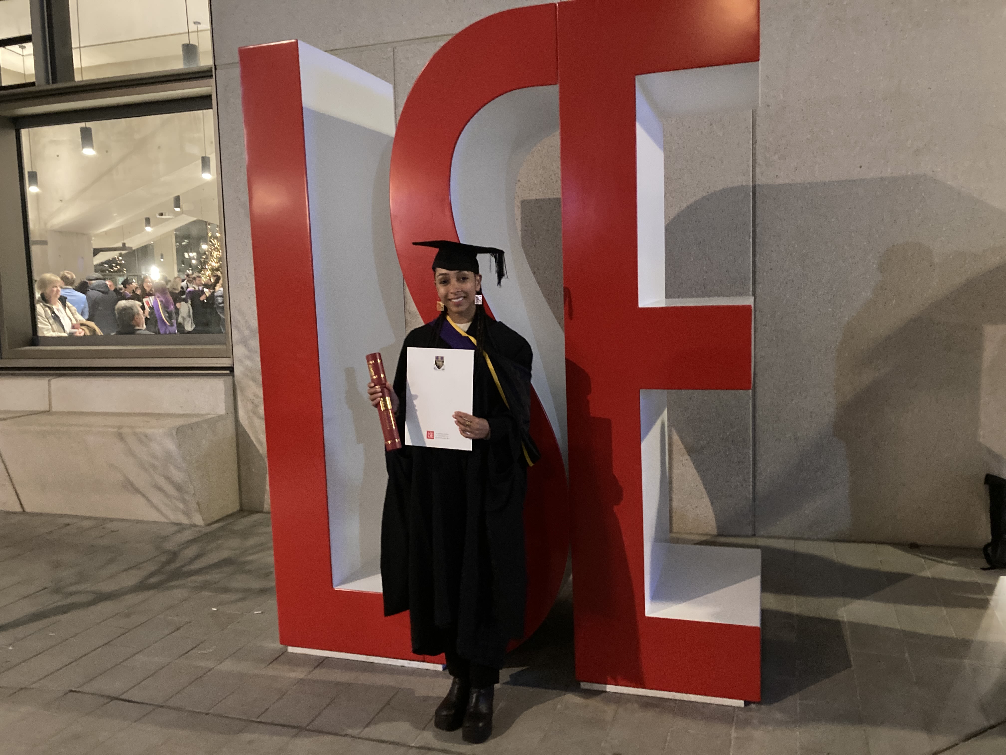 Phaedra Haringsma poses beside giant letters spelling LSE in her graduation robes