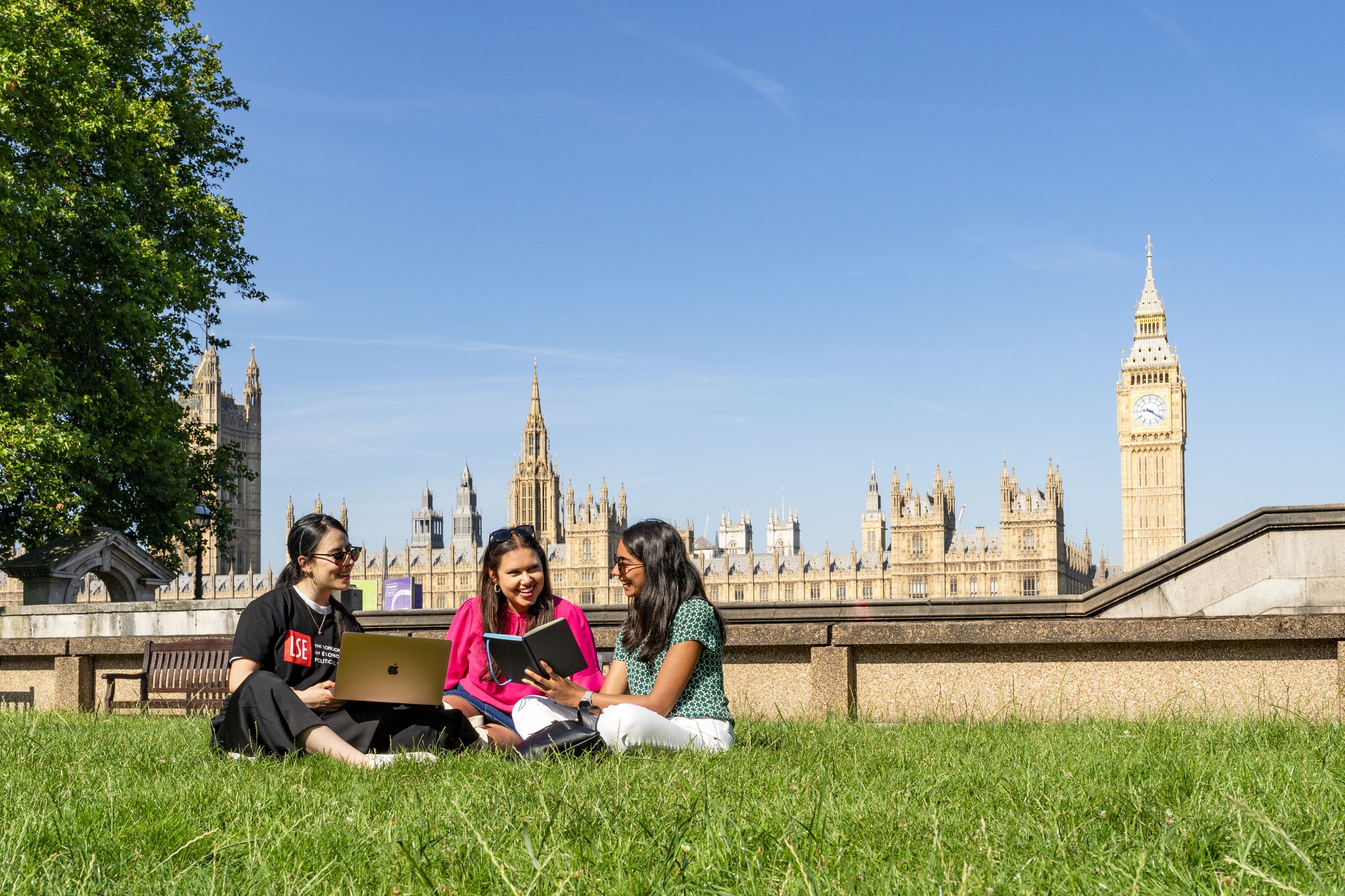 Three students sitting on the grass by the Thames River